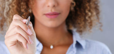A young woman holds a stylus and is pointing it at the screen as if to tap on something.
