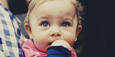 A man is holding a young baby who has a finger in her mouth