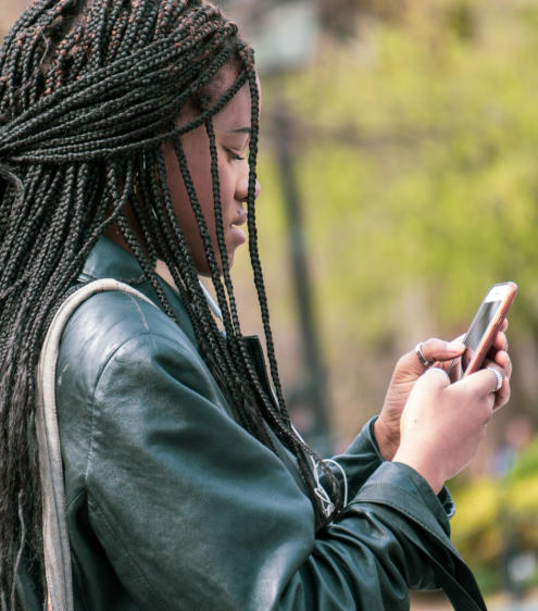 A young woman stands outside looking at her cell phone