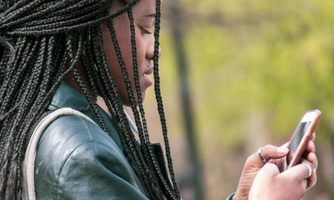 A young woman stands outside looking at her cell phone
